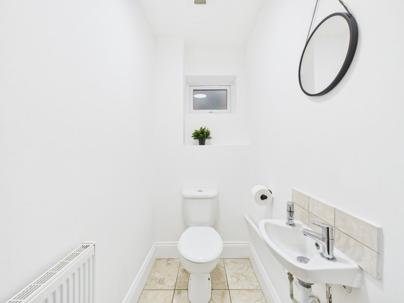 Small bathroom with toilet, wall-mounted sink, round mirror and potted plant on shelf