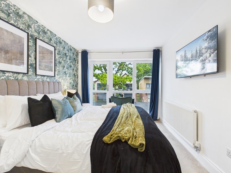 Modern bedroom with double bed, patterned wallpaper, blue curtains and wall-mounted TV