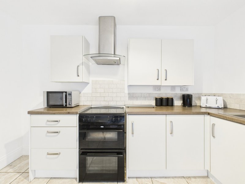 Modern kitchen with white cabinetry, black double oven, stainless steel range hood, and wood countertops