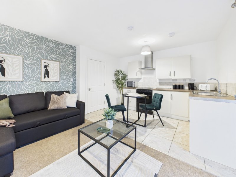 Open-plan living and kitchen area with dark sofa, dining table, white cabinetry and patterned feature wall