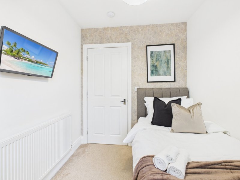 Compact bedroom with single bed, white door, wall-mounted TV and framed artwork
