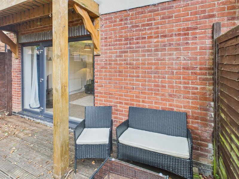 Brick patio area with wooden pergola, two dark rattan chairs with cushions, and glass door entrance