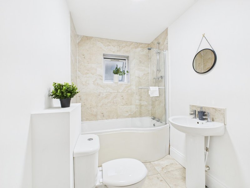 Clean bathroom with bathtub, toilet, sink, tiled walls and round mirror