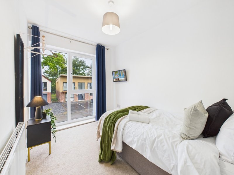 Bedroom with double bed, white bedding, green throw, navy curtains and glass doors to garden