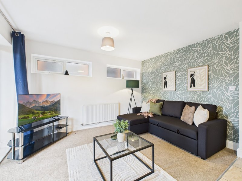 Modern living room with black sofa, TV, patterned wallpaper and glass coffee table