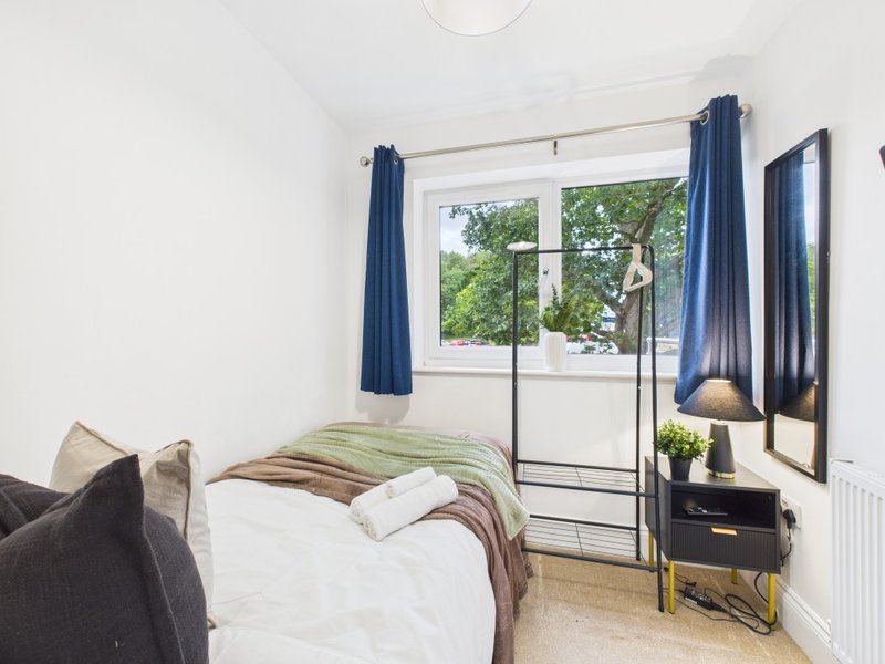 Bright bedroom with double bed, green bedding, blue curtains, wall-mounted TV and small black dresser