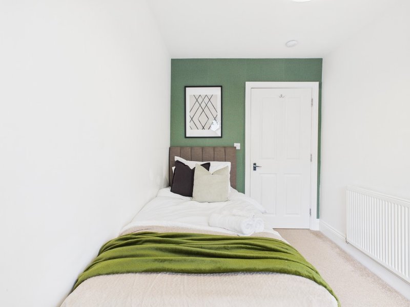 Modern bedroom with single bed, green accent wall, framed artwork and white door