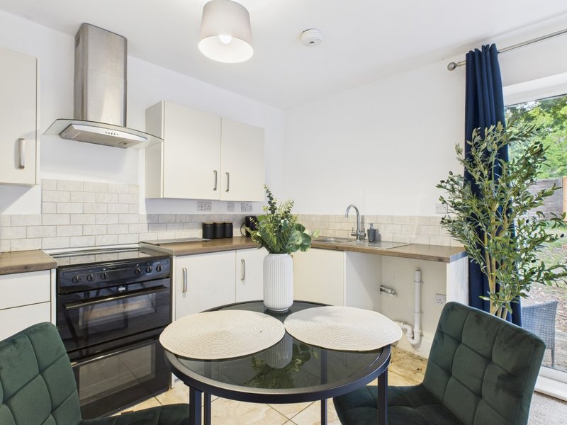 Modern kitchen with white cabinets, dining table, green plants and patio doors