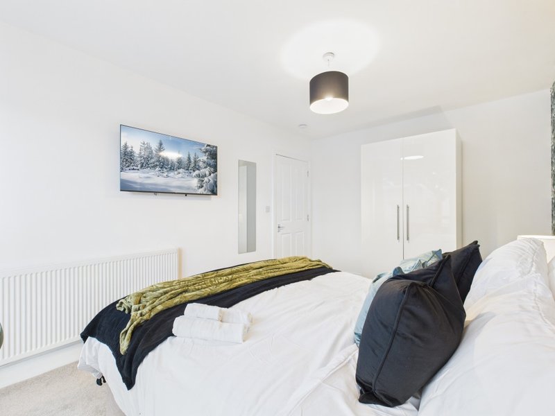 Bright bedroom with white bed, dark pillows, yellow throw, and framed winter landscape artwork