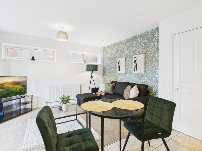 Modern living room with black sofa, green dining chairs, patterned wallpaper and wooden flooring