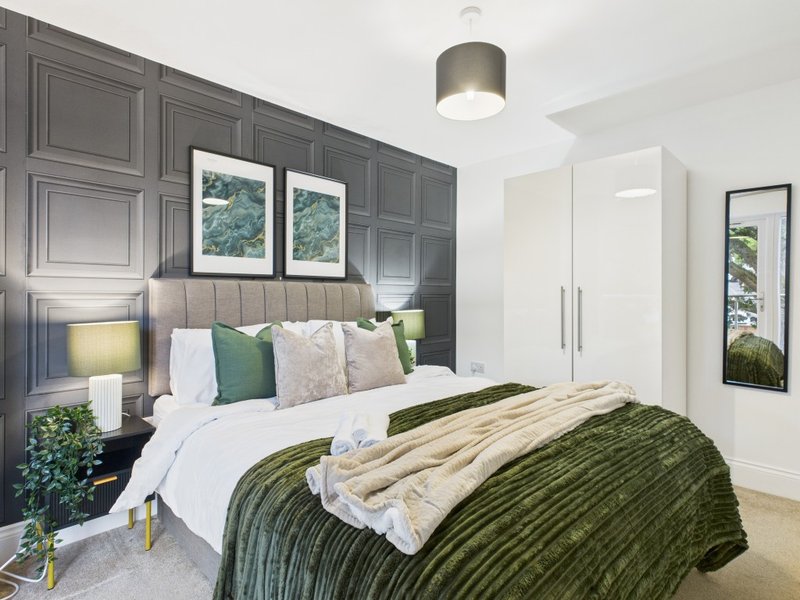 Modern bedroom with green upholstered bed, grey panelled headwall, framed artwork and pendant light
