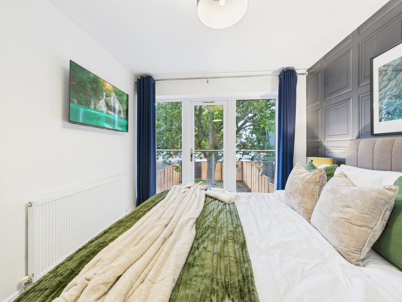Modern bedroom with double bed, green and white bedding, blue curtains, and French doors to balcony