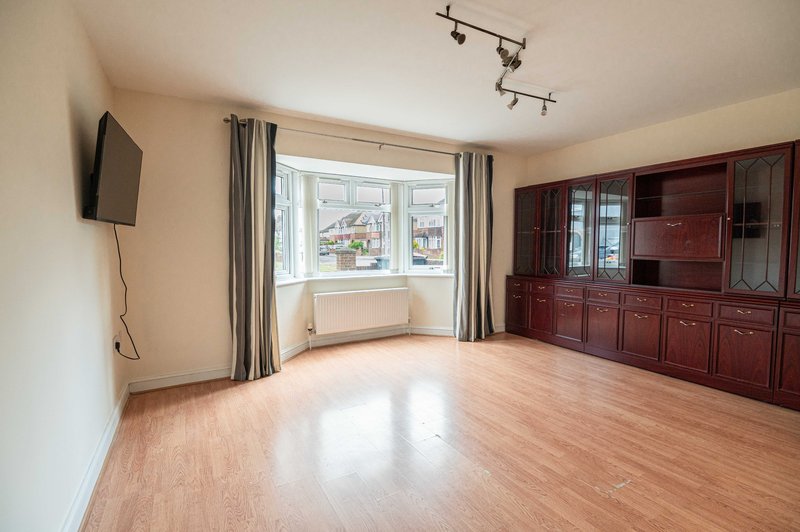 Spacious living room with wooden flooring, bay window, wall-mounted TV, and built-in dark wood cabinetry