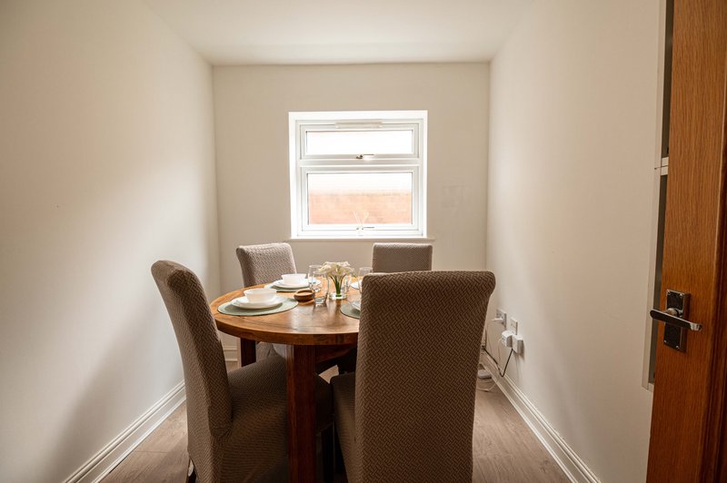 Small dining area with round wooden table, two upholstered chairs and window