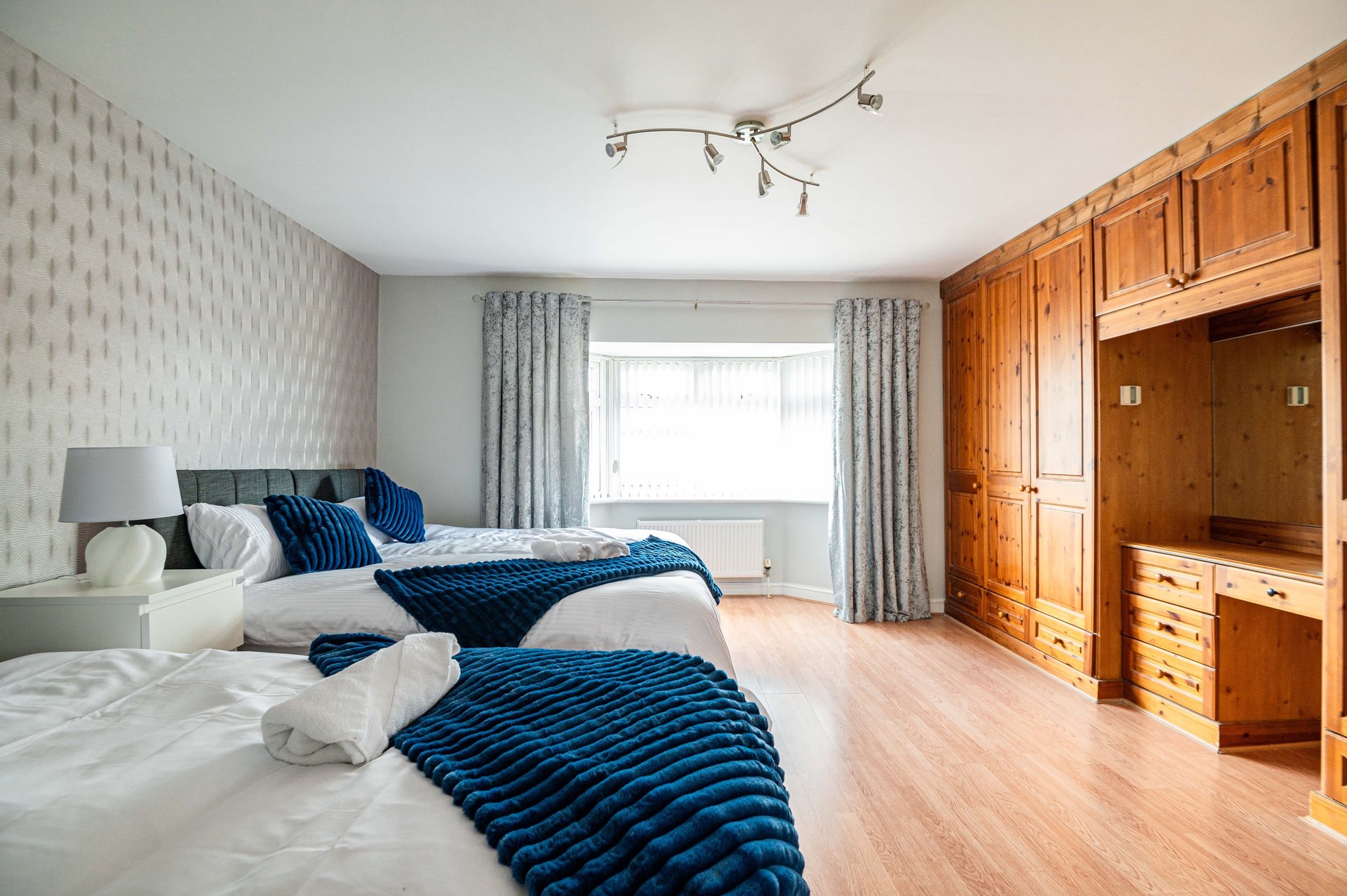 Spacious bedroom with two beds, wooden wardrobe, patterned wallpaper and window with grey curtains