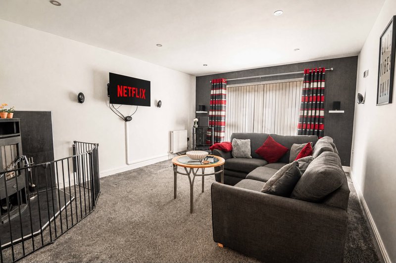 Modern living room with gray sofas, wall-mounted TV, round coffee table, and red checked curtains