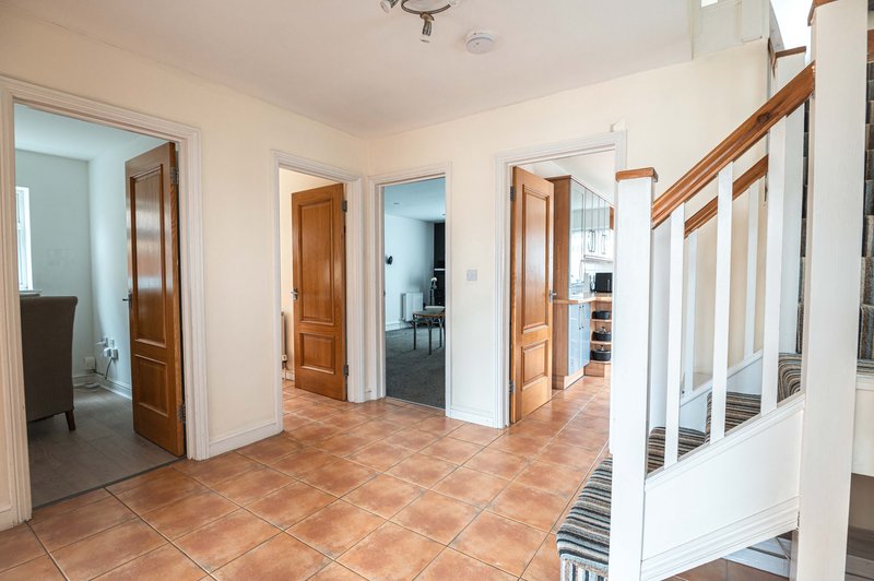 Spacious hallway with terracotta tile floor, wooden doors, and staircase with white railings