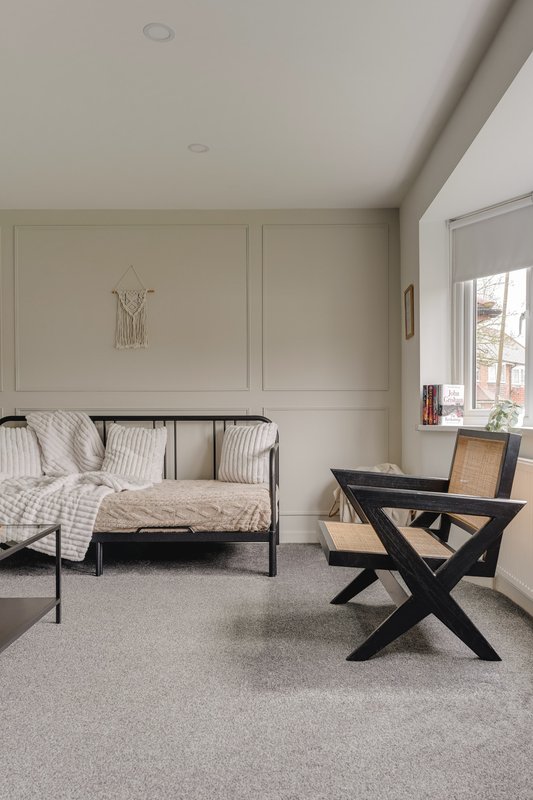 Bedroom with black metal bed frame, striped pillows, black X-frame chair and window