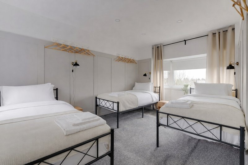 Bright bedroom with three single beds, metal frames, white bedding and pendant lights