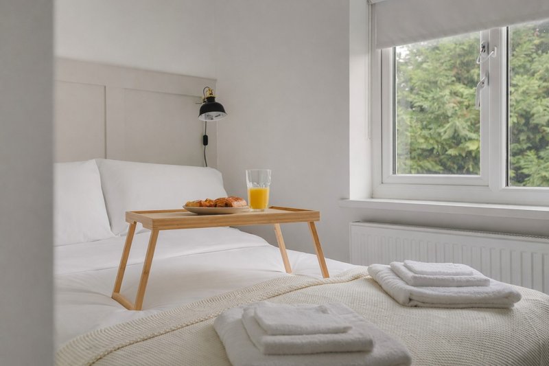 Bright bedroom with double bed, wooden breakfast tray, stacked towels and garden view