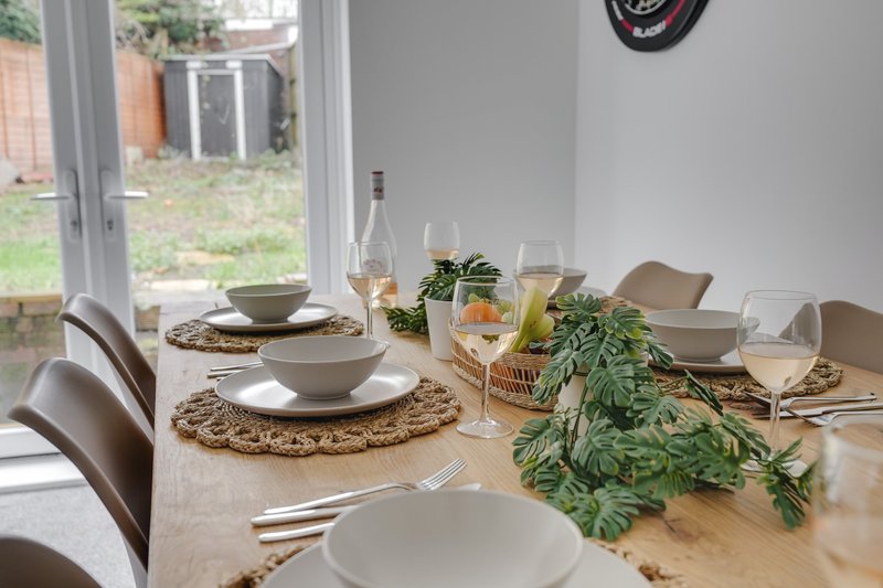 Wooden dining table set for meal with place settings, wine glasses, and plant centerpiece
