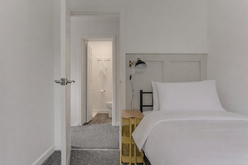 Bright bedroom with white bedding, wooden bed frame, and open doorway to bathroom