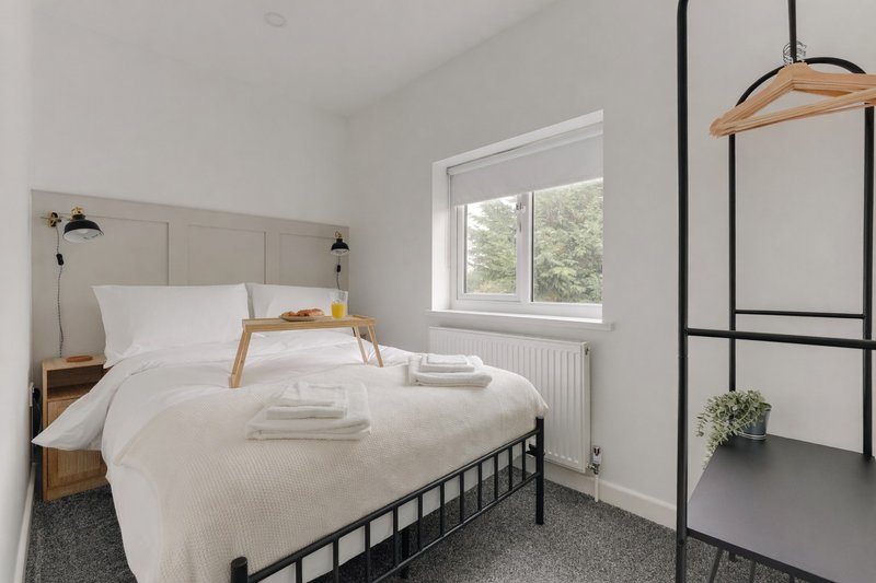 Bright bedroom with metal-frame bed, white bedding, wooden nightstand and pendant lamps