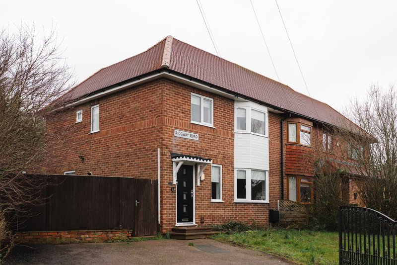 Brick semi-detached house with brown metal roof, driveway, garage and front garden