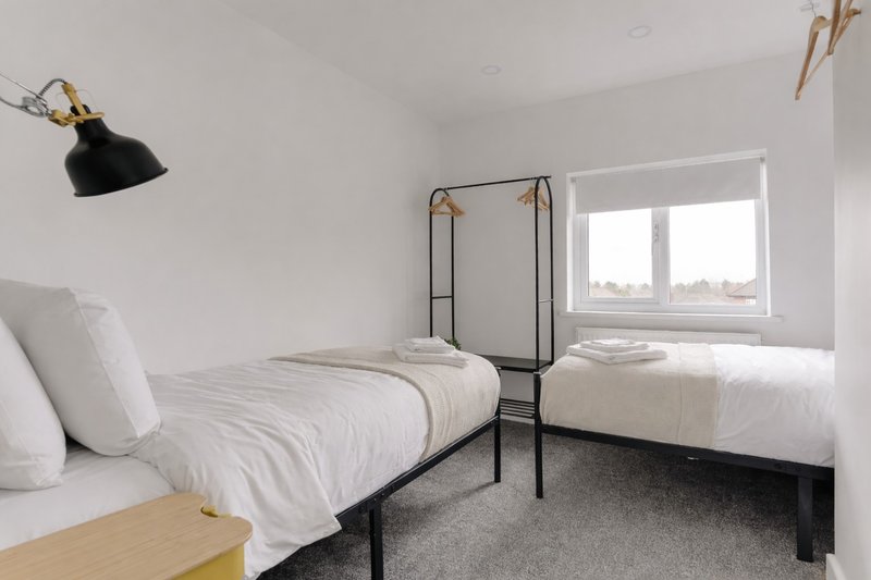 Modern twin bedroom with two single beds, black metal frames, white bedding, and bright window