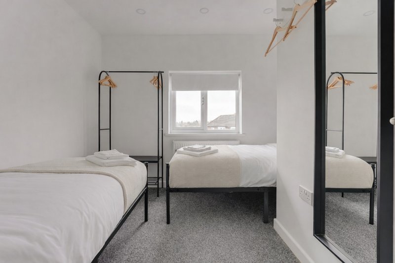 Modern bedroom with two single metal-frame beds, white bedding, window and grey carpet flooring