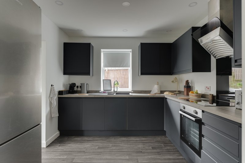 Modern kitchen with black cabinetry, stainless steel appliances, and window overlooking garden