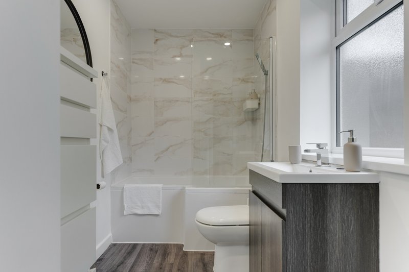 Modern bathroom with marble shower enclosure, dark vanity, white toilet and towel rail