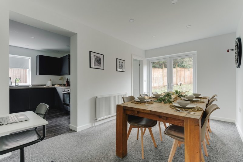 Open-plan dining and kitchen area with wooden table, chairs, and windows overlooking garden