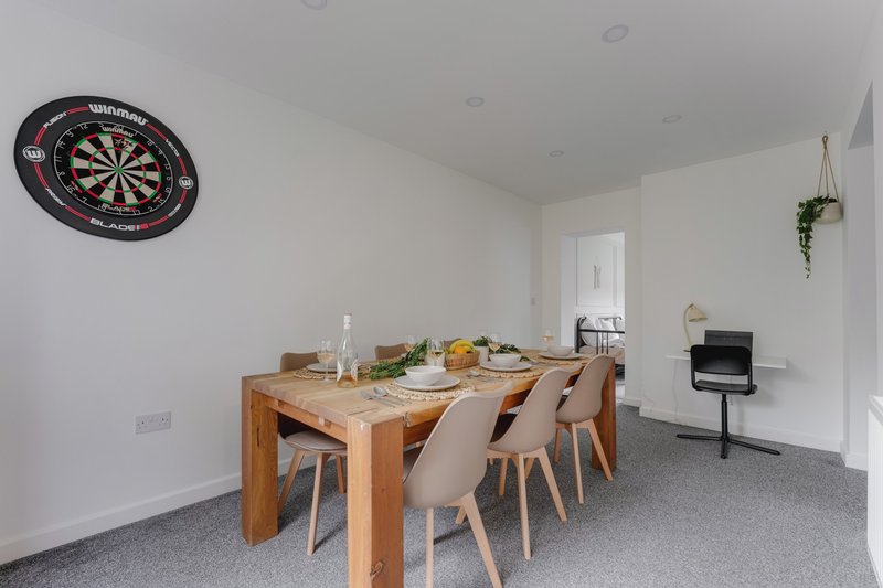 Open-plan dining area with wooden table, chairs, dartboard wall decoration, and potted plant