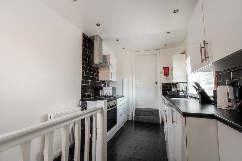 Galley kitchen with white cabinets, black countertops, black tile splashback and dark flooring