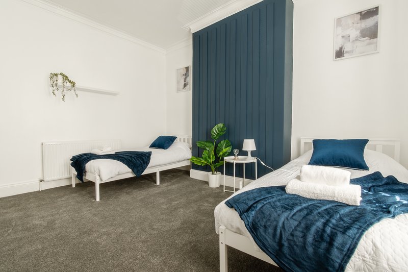 Bright bedroom with two single beds, dark blue bedding, white walls and teal curtains