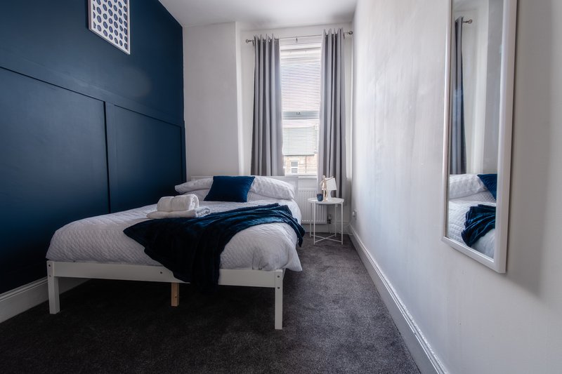 Modern bedroom with double bed, navy headboard, grey carpet and mirrored wardrobe