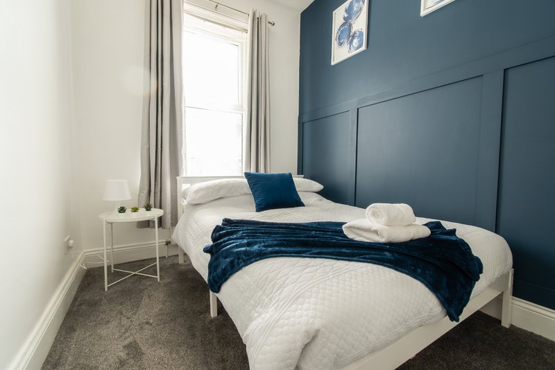 Modern bedroom with double bed, blue headboard, white bedding and navy throw blanket