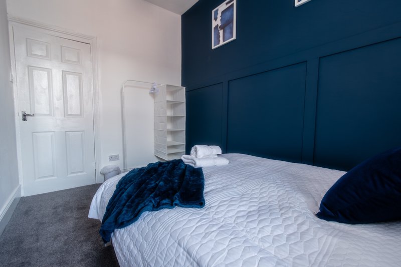 Modern bedroom with double bed, dark blue feature wall, white door and grey carpet