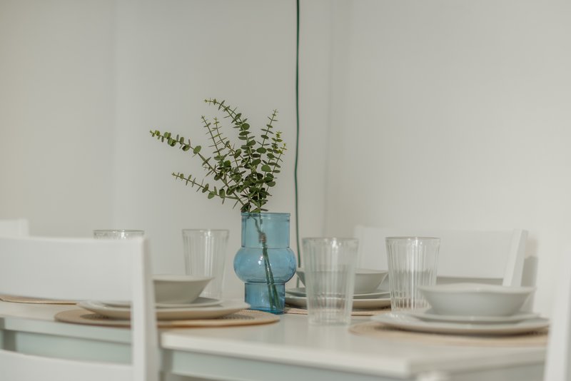 Minimalist dining table with place settings, glasses, and blue vase with eucalyptus stems
