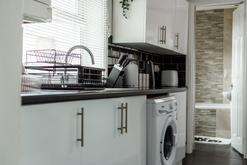 Modern kitchen with white cabinetry, black countertop, dish rack, washing machine and window blinds