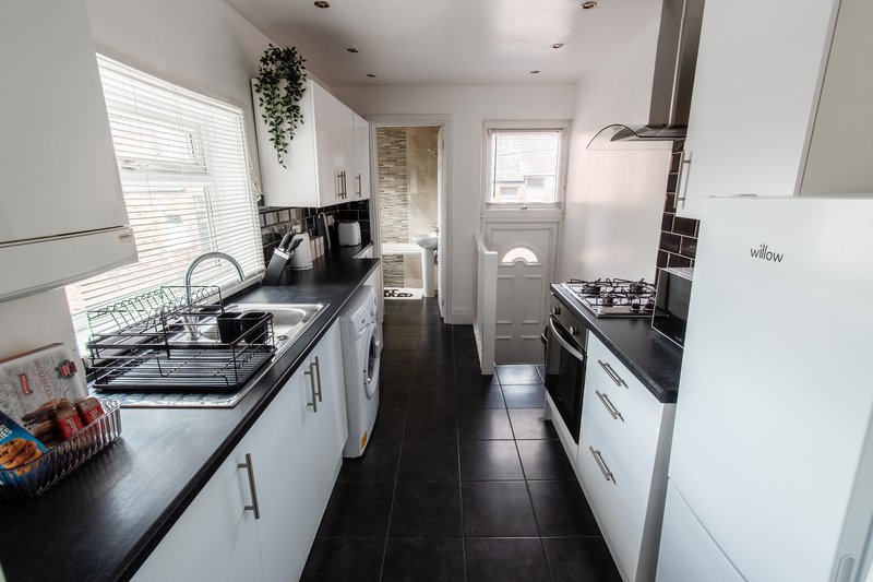 Modern galley kitchen with white cabinetry, black countertops, stainless steel appliances and dark floor