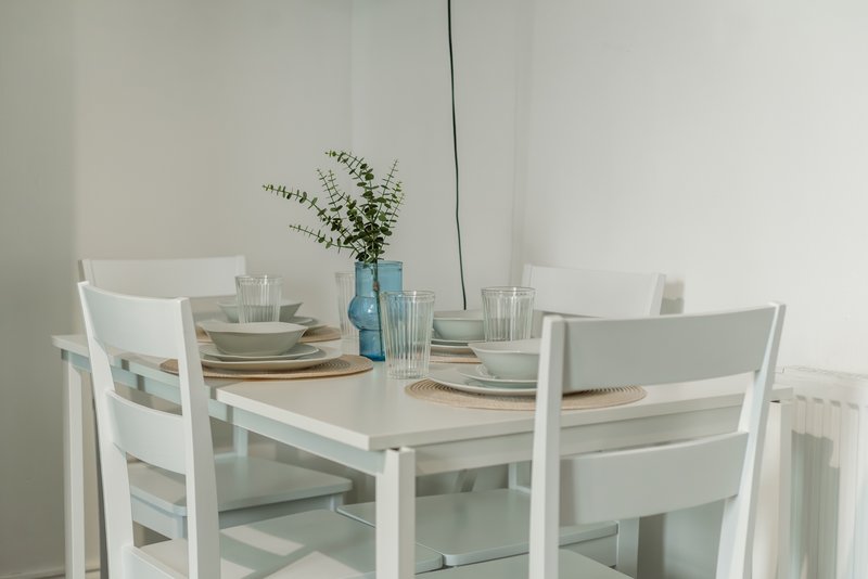 Minimalist dining room with white table, chairs, place settings and blue vase with greenery