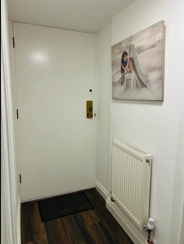 Narrow hallway with wooden floor, white door, radiator and wall art