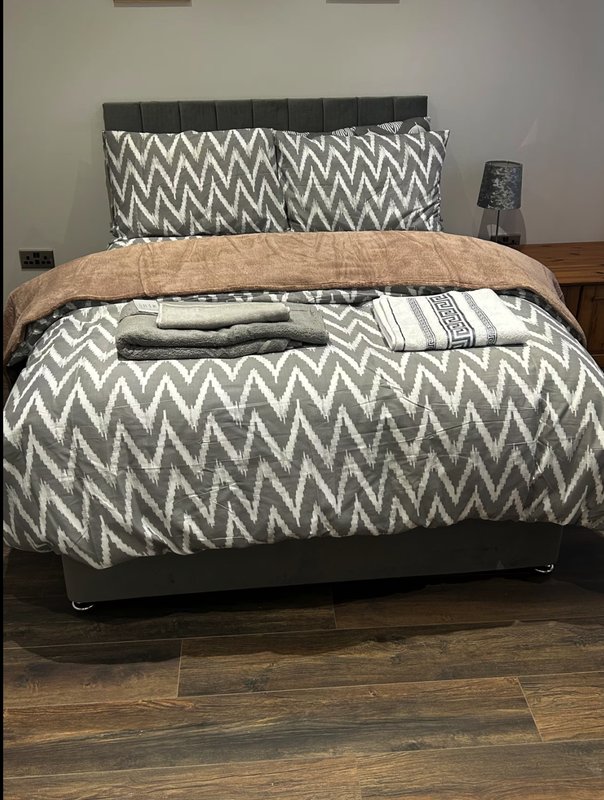 Bedroom with double bed, patterned bedding, tan throw blanket, and wooden floor