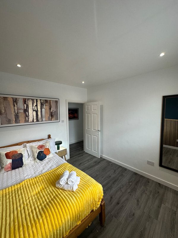 Bright bedroom with yellow bedspread, wooden flooring, white walls and recessed lighting