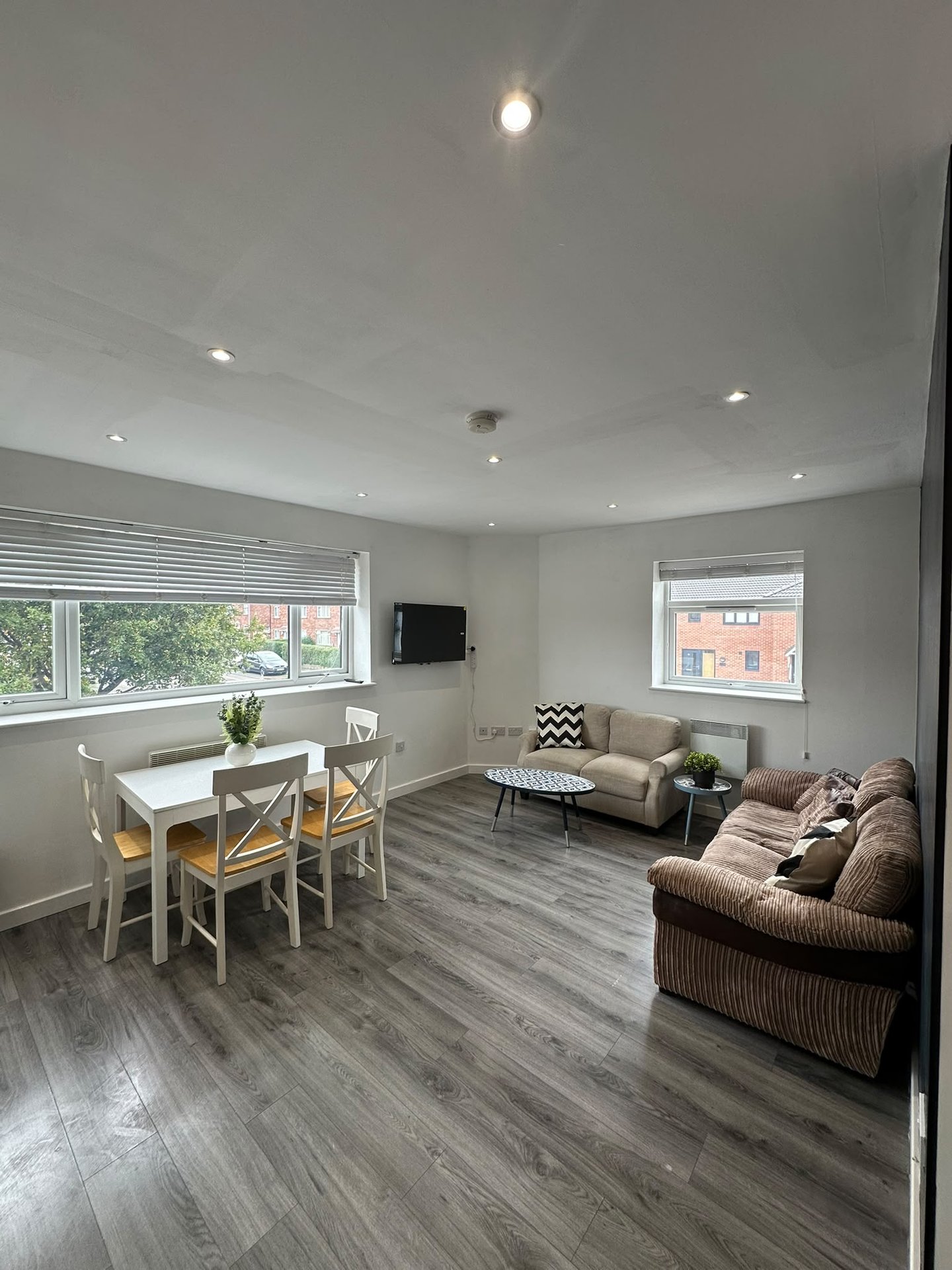 Modern open-plan living room with dining table, sofa seating, and large windows overlooking street