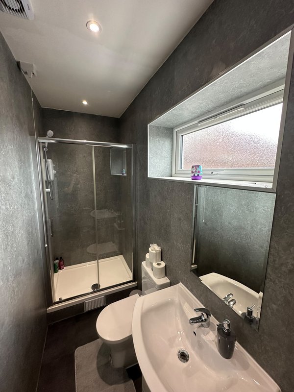 Modern bathroom with shower enclosure, toilet, white sink and dark gray tiled walls