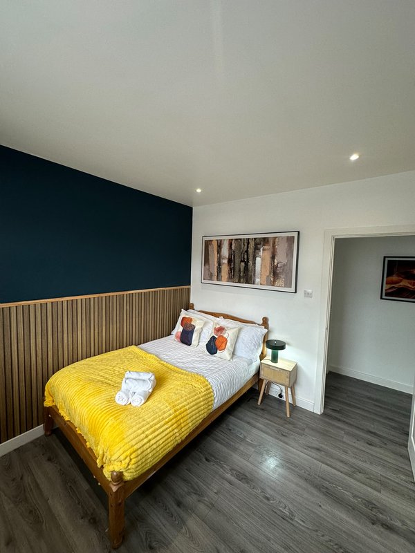 Modern bedroom with yellow duvet, wooden bed frame, dark feature wall and white pillows