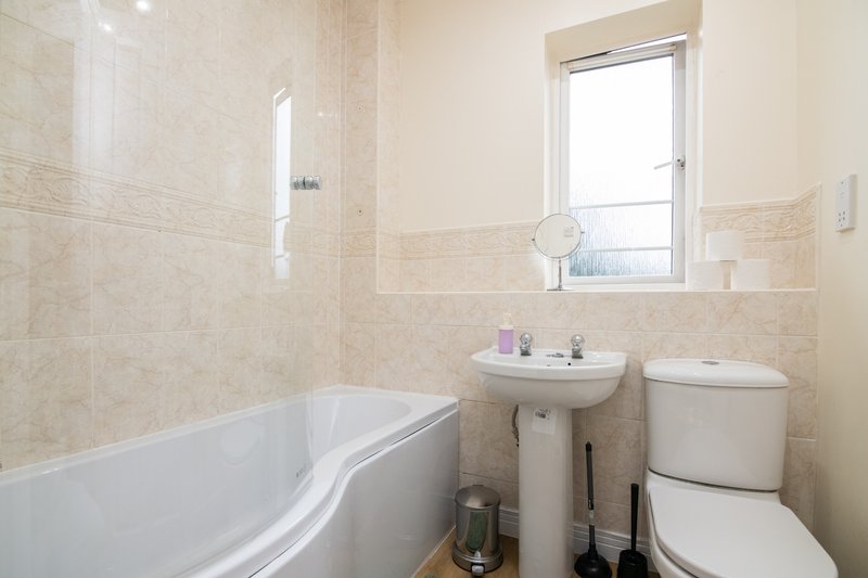 Clean bathroom with bathtub, pedestal sink, toilet, and window with natural light